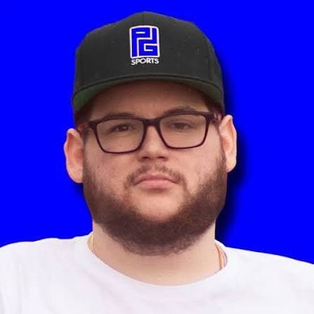 Bearded man wearing glasses and a black PG Sports baseball cap against a blue background.
